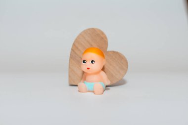 Minyatür bir kalp, yeni doğmuş bebek oyuncağı beyaz gri bir arkaplanda oturuyor. Odaklan, boşluğu kopyala.