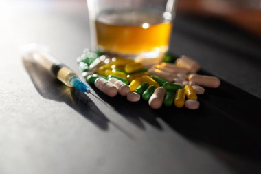 Koyu gri masada sert uyuşturucu ve alkol. Alkol hapları. Plastik kokain torbası. Masada gölgeli..