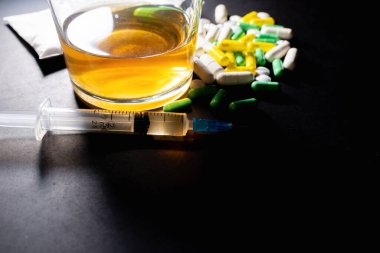 Koyu gri masada sert uyuşturucu ve alkol. Alkol hapları. Plastik kokain torbası. Masada gölgeli..