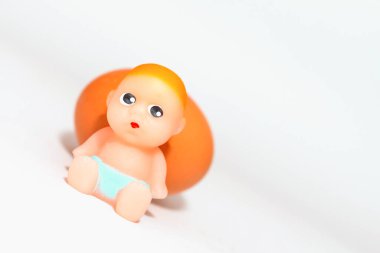Minyatür yeni doğmuş bebek oyuncağı ve yumurta beyaz gri bir arkaplanda oturuyor. Odaklan, boşluğu kopyala.