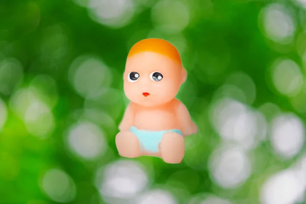 Miniature Newborn Baby Toy Sitting Green Blurred Foliage Isolated Background — Stok fotoğraf