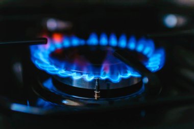 Evdeki bir gaz sobasından gaz yanıyor. Mavi yansımalı gaz alevi. Yakın çekim, seçici odaklanma..