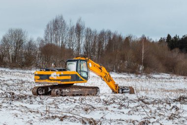 Karlı bir kış ormanı manzarasında sarı kazıcı. Kış ormanlarının arka planında kazıcılar. İnşaat alanının hazırlanması.