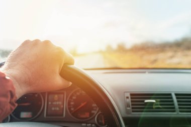 Araba, yol, direksiyondaki erkek sürücünün eli, bulutlu gün batımı gökyüzü, arka plan. Kapan, seçici odaklan. Gün batımı manzarası..