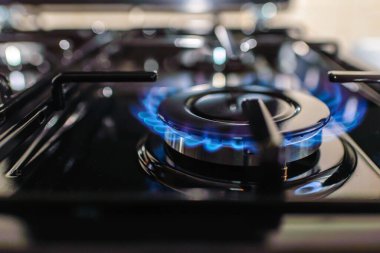 Evdeki bir gaz sobasından gaz yanıyor. Mavi yansımalı gaz alevi. Yakın çekim, seçici odaklanma..