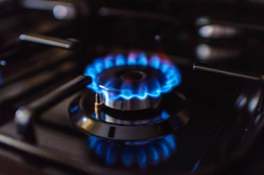 Evdeki bir gaz sobasından gaz yanıyor. Mavi yansımalı gaz alevi. Yakın çekim, seçici odaklanma..