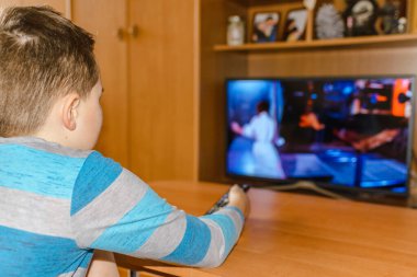 Genç çocuk film izliyor ve uzaktan kumandayı evde televizyon ekranının yanında tutuyor. Seçmeli odak, arka plan resmi.