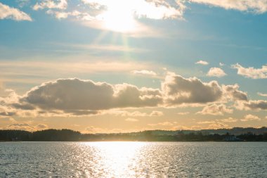 Gölün üzerinde bulutlu bir gökyüzünde güzel bir günbatımı. Sahilde ağaçlar var. Manzara harika..