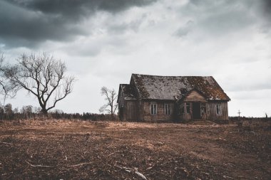 Terk edilmiş eski bir ahşap korku evi, sonbahar akşamları ağaçlı dramatik fırtınalı bulutlar..