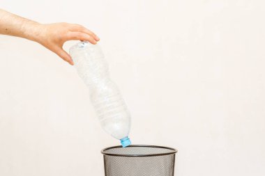 Plastik şişe çöp kutusuna atılıyor. Beyaz, gri arka plan, seçici odak, kopyalama alanı..