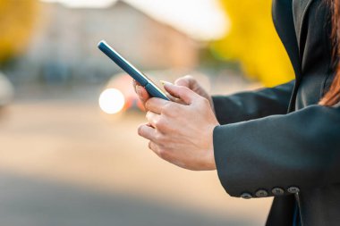 Sokakta akıllı telefon kullanan bir iş kadını. Arka planda bulanıklık var. Yakın plan..