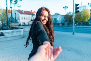 Yüzünde gülümseme olan mutlu esmer kız gün batımında erkek arkadaşının elini tutuyor ılık bir bahar, yaz akşamında. Beni takip et kavramı..