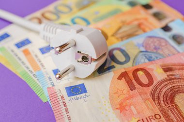 Elektrik prizi, Avro Kağıt Para Banknotları. Kapalı alanda mor arka plan. Tüm konut ve işyeri kullanıcıları için elektrik maliyetlerinin artırılması, pahalı enerji faturası ve elektrik fiyatları kavramındaki artış.