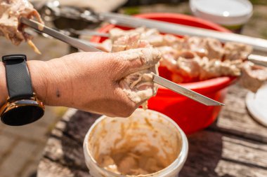 Kadın eli alüminyum metal havzadan tükürüğe çiğ domuz eti sokuyor, açık havada poultru shashlik pişiriyor. yaz güzel gün.
