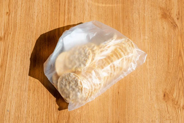 Round rice or corn cakes in a transparent plastic bag lie on the floor. Packaging of healthy snack. Selective focus.Top view.