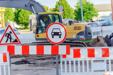 Büyük bir traktör, yolu kapatan sarı bir kazıcı, yol işaretli bir yol..