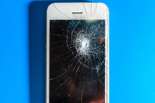 crashed smartphone with broken black screen on blue background. Top view. Repair concept.