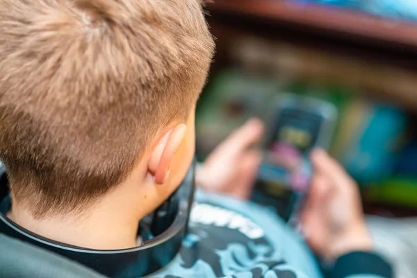 A boy 10s watches a video clip in a smartphone at home. Back view,closeup.Selective focus.