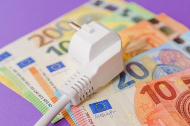 Elektrik prizi, Avro Kağıt Para Banknotları. Kapalı alanda mor arka plan. Tüm konut ve işyeri kullanıcıları için elektrik maliyetlerinin artırılması, pahalı enerji faturası ve elektrik fiyatları kavramındaki artış.
