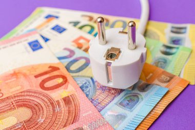 Elektrik prizi, Avro Kağıt Para Banknotları. Kapalı alanda mor arka plan. Tüm konut ve işyeri kullanıcıları için elektrik maliyetlerinin artırılması, pahalı enerji faturası ve elektrik fiyatları kavramındaki artış.