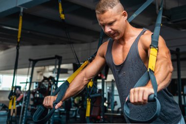 Genç ve güçlü bir adam spor salonunda trx fitness kayışlarıyla şınav çekiyor. Yaklaş..