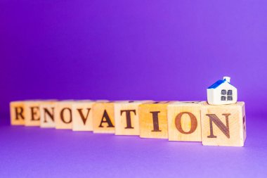 Renovation symbol. Wooden cubes with the word RENOVATION, miniature toy house.Purple,veri peri color background. Business and renovation concept. Copy space.