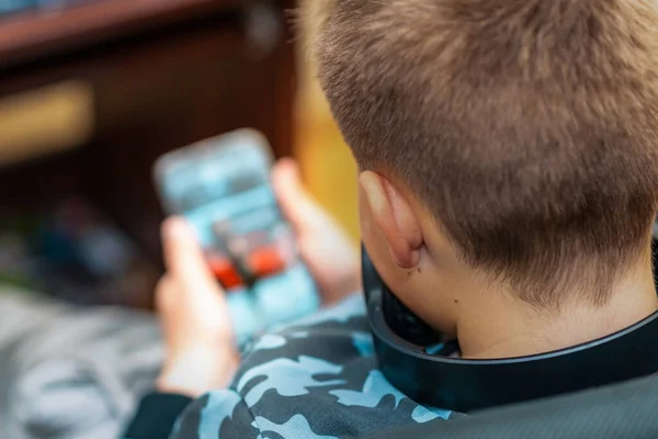 A boy 10s watches a video clip in a smartphone at home. Back view,closeup.Selective focus.