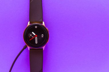 Smartwatch şarj oluyor. Kablosuz şarj göstergesiyle kablosuz şarj cihazını izle. Üst görünüm. Metin için yer. Bulanık mor, veri peri renk arkaplanı. Kopyala boşluk. Telsiai, Litvanya.07-01-2022.