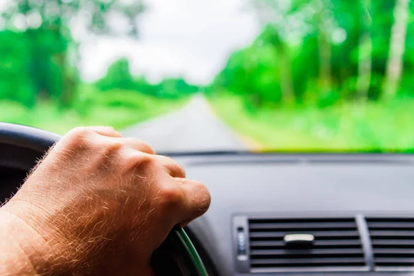 View of the road through the windshield of the car.Driver\'s hand on steering wheel at forest rainy summer blurred background. Driving,travel car concept.