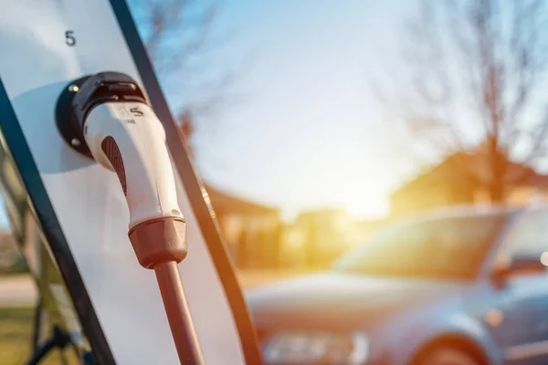 Close up power cord for electric car. Green station.Power supply for electric car battery charging.Blurred car,sunset in the background.Selective focus.Closeup.