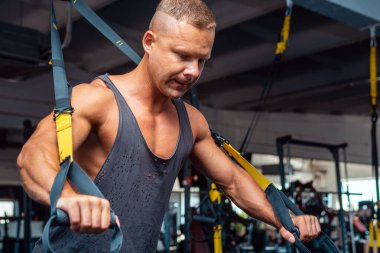 Genç ve güçlü bir adam spor salonunda trx fitness kayışlarıyla şınav çekiyor. Yaklaş..
