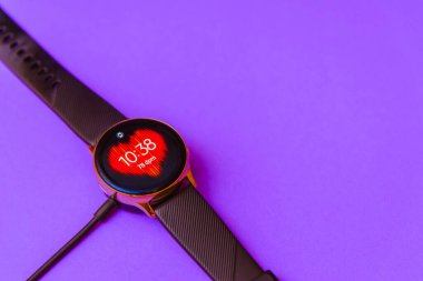 Smartwatch şarj oluyor. Kablosuz şarj göstergesiyle kablosuz şarj cihazını izle. Üst görünüm. Metin için yer. Bulanık mor, veri peri renk arkaplanı. Kopyala boşluk. Telsiai, Litvanya.07-01-2022.