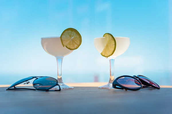 Two drinking glasses of Margarita cocktails. Beach bar concept. Summer alcoholic cocktails,sunglasses on table bar, sea on background.