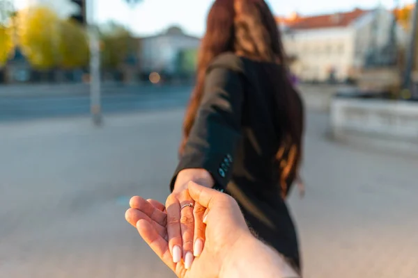 Happy brunette girl turn away face holding boyfriend\'s hand on a street at sunset on a warm spring,summer evening.Follow-me concept.Selective focus.