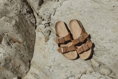Kayalıklarda bir çift sandalet. Gün boyunca kayaların üzerinde bir çift kahverengi sandalet..