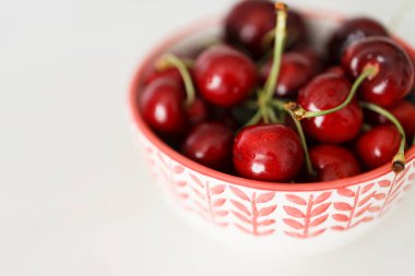 Sweet cherries in a  bowl on white table and light background.Bowl of fresh red cherries on white background