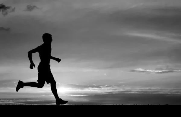 Silueta de hombre corriendo sobre fondo ardiente puesta de sol. Negro y blanco — Foto de Stock