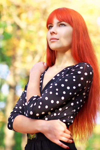 Schönes Mädchen mit roten Haaren steht im Herbst in einem Park — Stockfoto