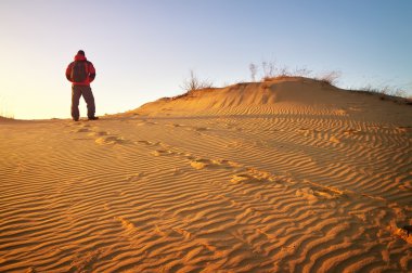 Sandy çöl ve kış giysileri dune tepesinde duran adam