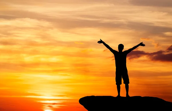 Silhouette of a man on a mountain top on fiery orange background — Stock Photo, Image