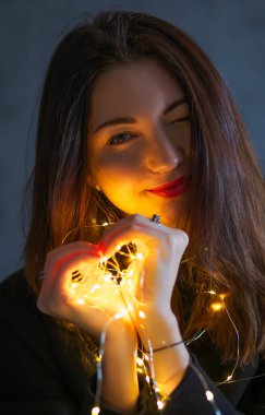 Noel çelengi takan bir kız. Ellerinde ışık, kalp şeklinde.