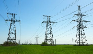 Güneşli bir günde mavi gökyüzünde bulutlar olan düz ve yeşil tarım arazisindeki yüksek voltaj hatları ve elektrik direkleri. Bulutlu ve yağmurlu. Buğday büyüyor.