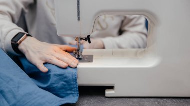 Terzi kız çalışıyor, dikiş makinesine elbise dikiyor, elleri yakın plan. Atölyede ya da atölyede dikiş dikme işlemi. Terzilik ve giysi tamiri. Serbest çalışan..