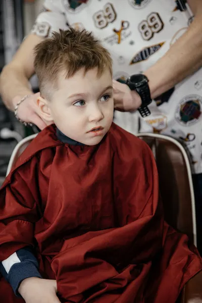 Uroczy pięciolatek strzyże się u fryzjera. Fryzjer układa włosy niemowlętom. Sklep fryzjerski. Dzieciństwo. Nowa fryzura dla małego chłopca. — Zdjęcie stockowe