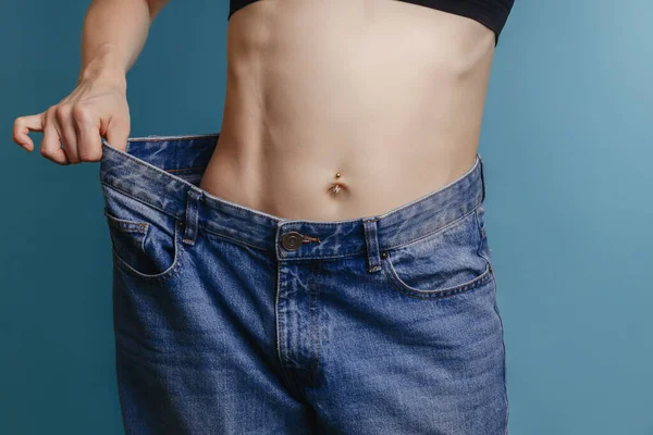 幅広のジーンズと白いシャツを着た30代の魅力的で細身の若い女性は、体重減少が成功していることを示しています。ダイエットと減量の概念.脂肪吸引. — ストック写真