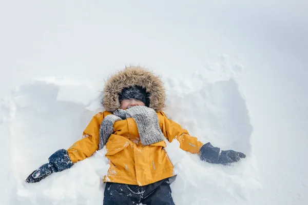 Niño feliz es un niño jugando en un paseo de invierno en la naturaleza. Un niño hace un ángel de nieve. — Foto de Stock