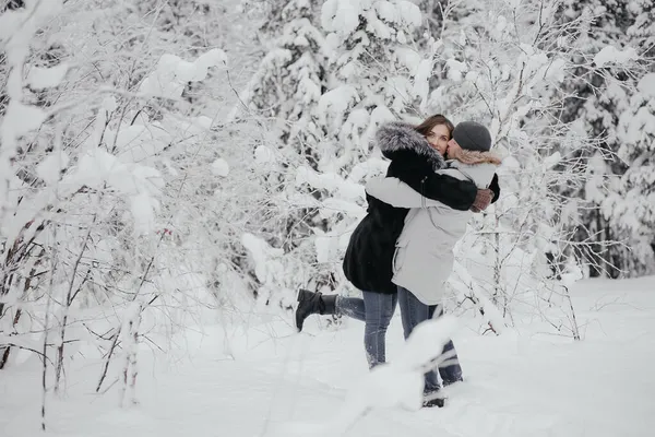Beautiful young European couple in a sweater in winter in the forest hugging, kissing. Man and woman, travel, nature. In love, girlfriend. Christmas holidays, recreation at the base. — Stock Photo, Image