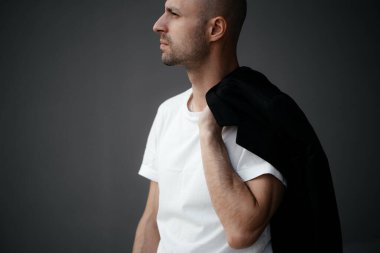 Beyaz tişörtlü, gri arka planda yakışıklı, kel bir adamın resmi.