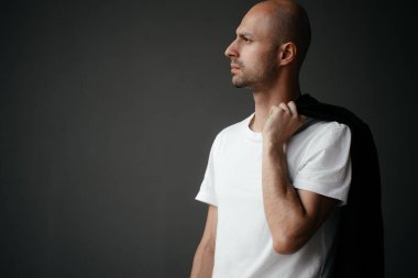 Beyaz tişörtlü, gri arka planda yakışıklı, kel bir adamın resmi.