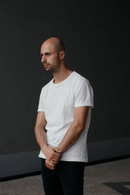Beyaz tişörtlü, gri arka planda yakışıklı, kel bir adamın resmi.